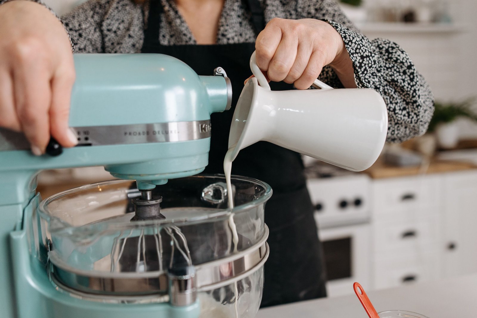 Person pouring ingredients into a stand mixer bowl while baking
