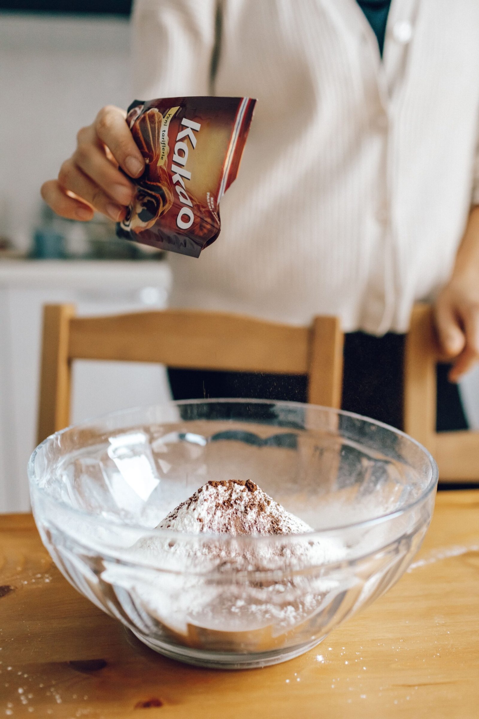 person adding cocoa powder to a baking mix in a bowl