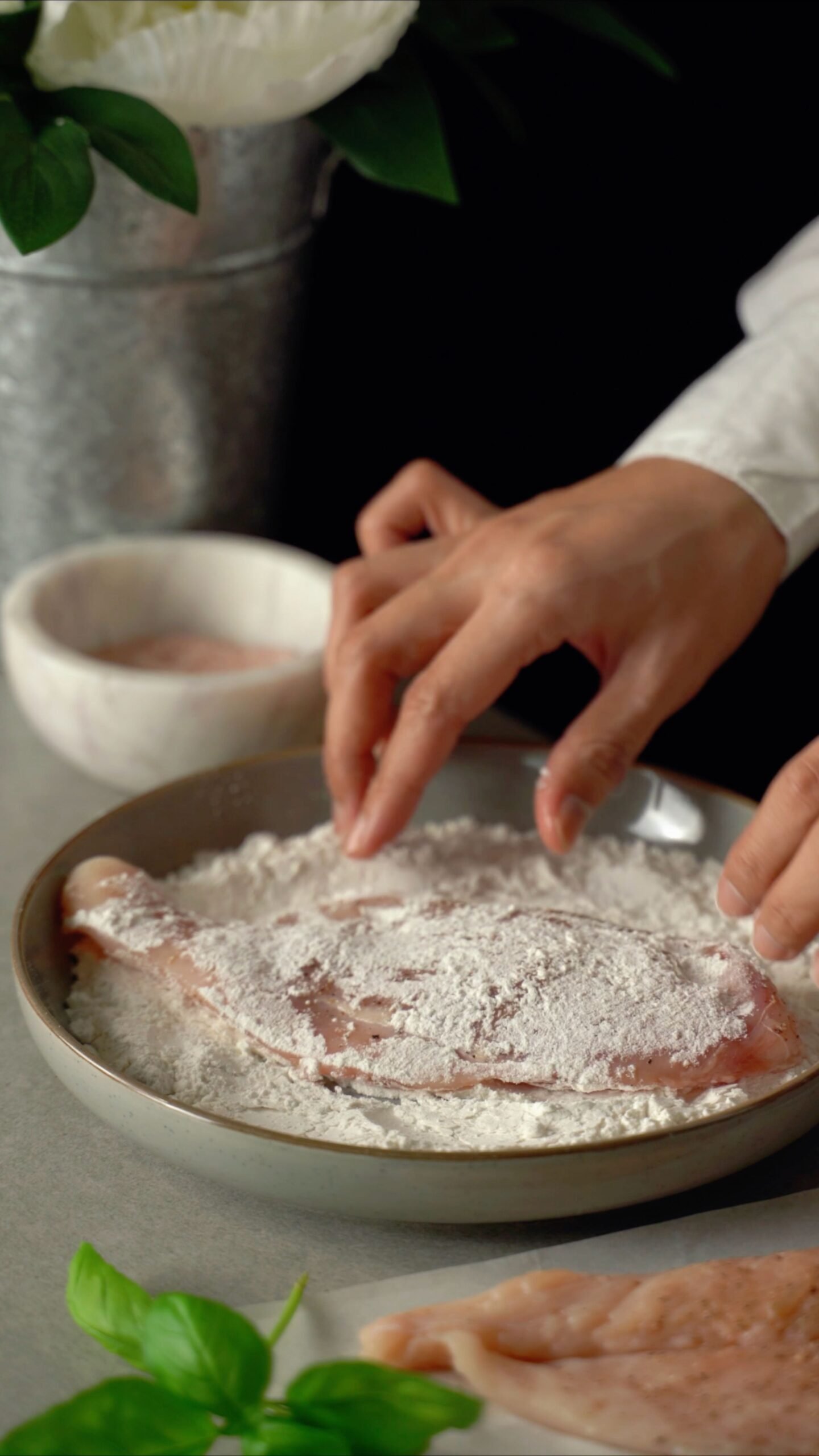 Hands coating raw chicken pieces in seasoned flour for breading