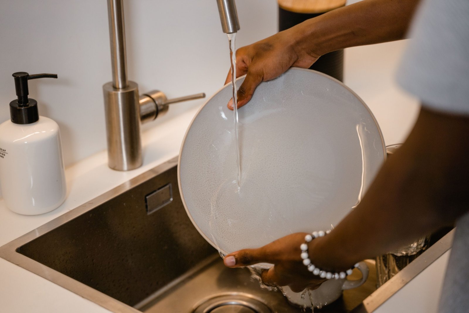 person washing a plate at the kitchen sink near the faucet used for a portable dishwasher hookup