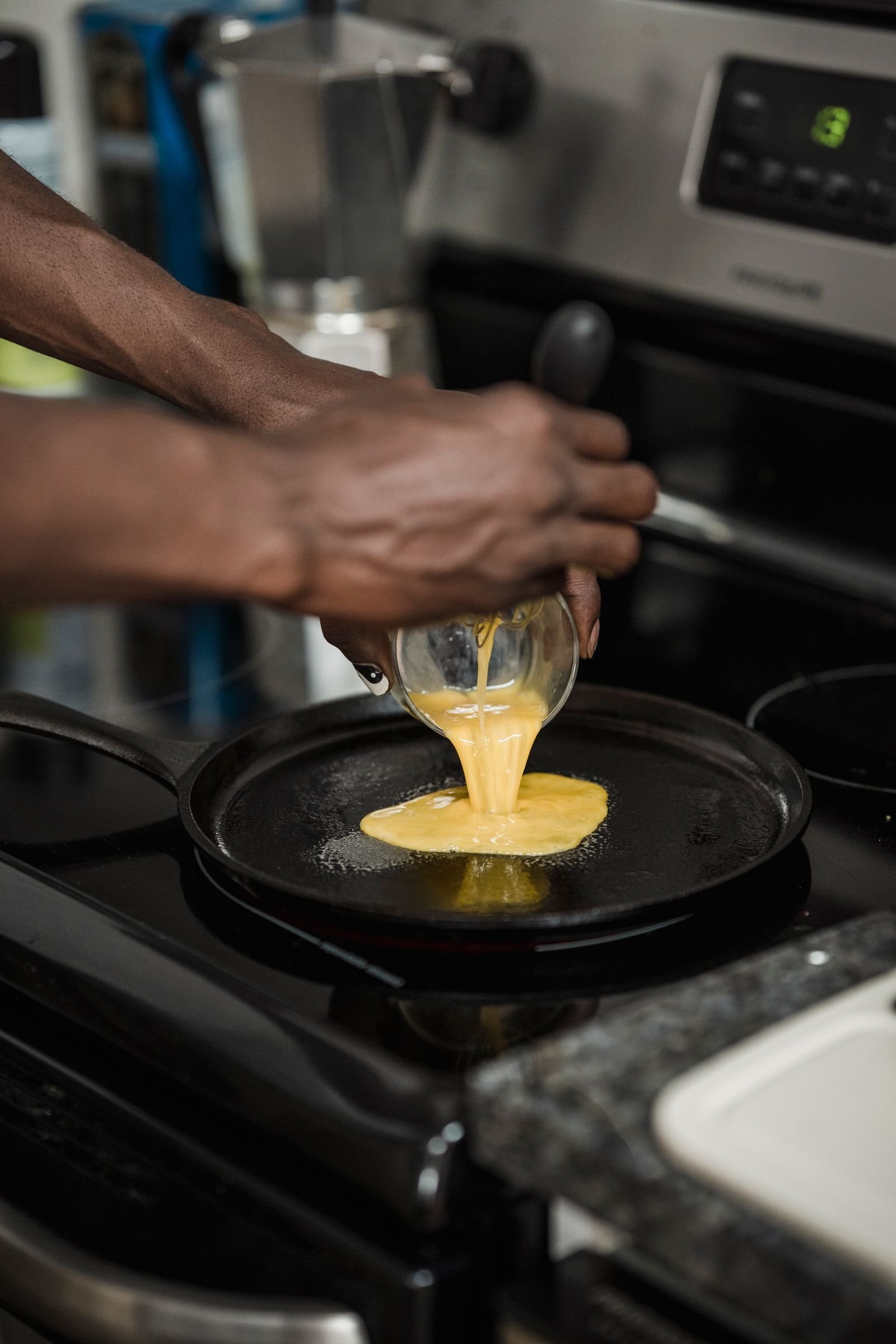 hands pouring whisked eggs into a nonstick frying pan on a kitchen stove