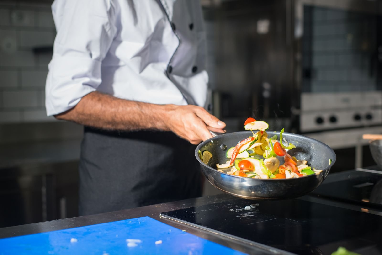 chef cooking vegetables in a nonstick frying pan on a modern stovetop