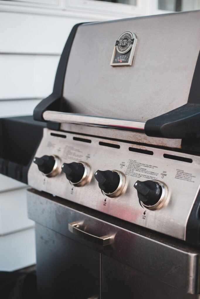 Close-up of a stainless steel gas grill with control knobs before cleaning