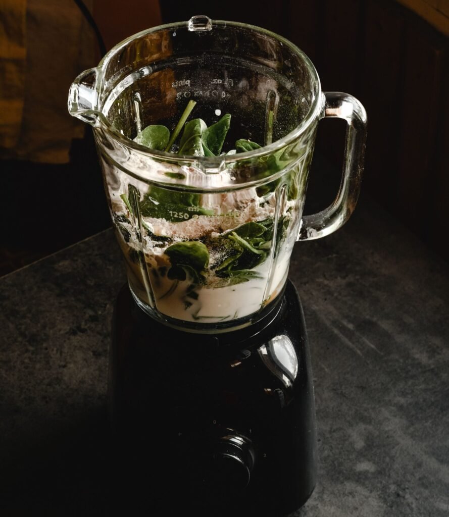 close-up of a blender container with fresh green smoothie ingredients on a kitchen counter
