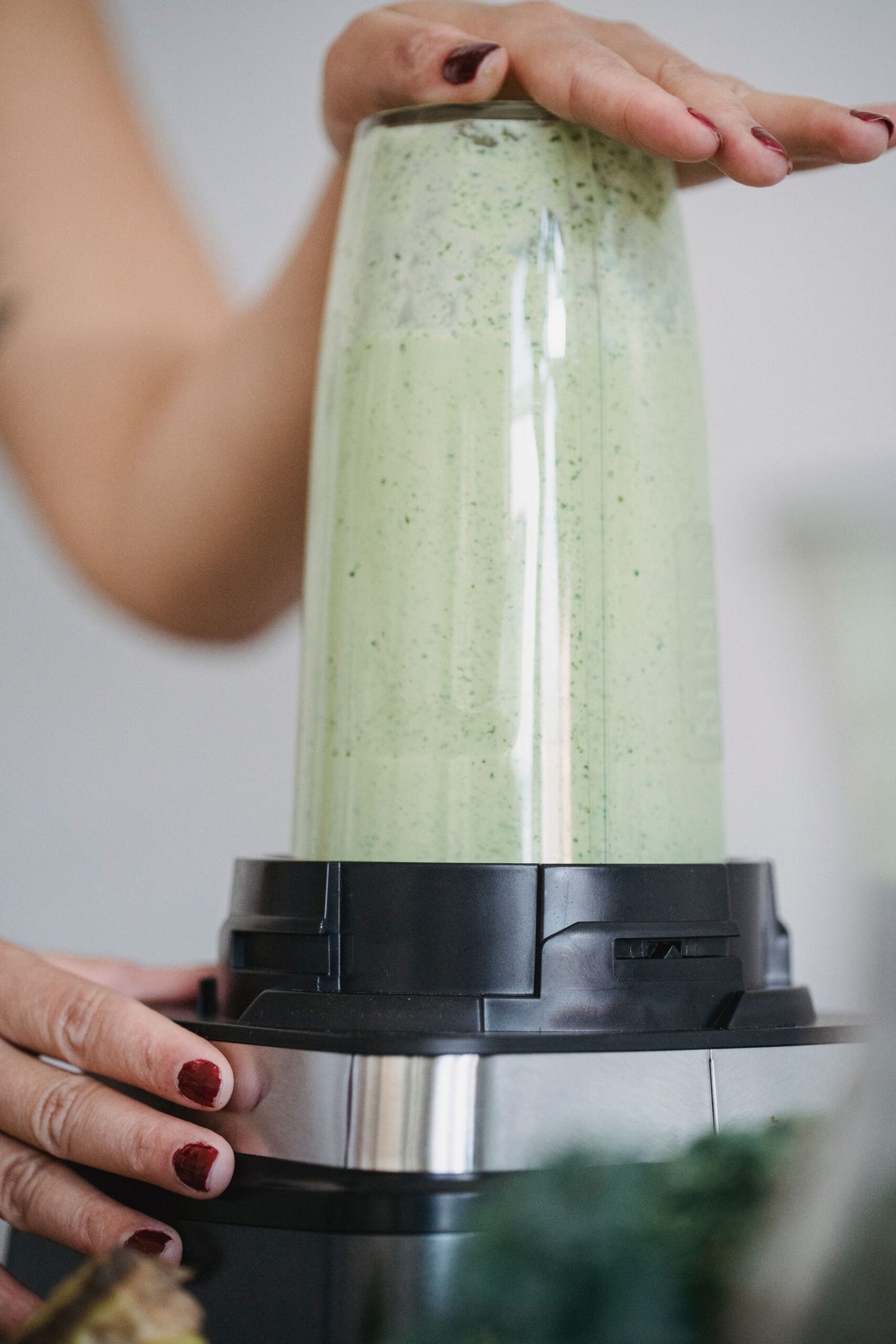 hands blending a green smoothie in a high-powered blender