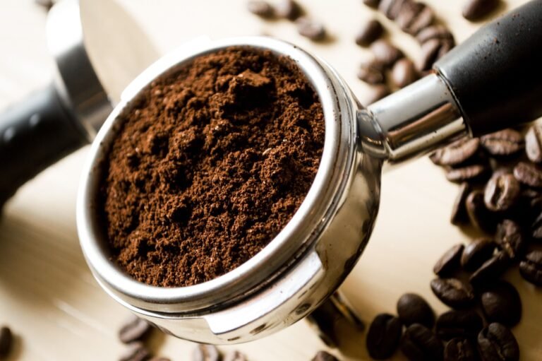 scoop of ground coffee next to whole coffee beans for measuring