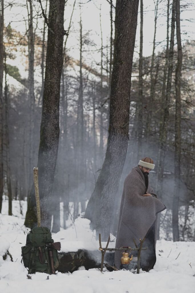 person at a snowy wilderness campsite with a campfire for melting snow into drinking water