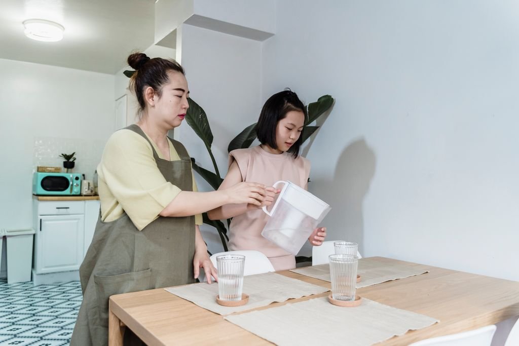 mother and daughter filling a glass filter jug with drinking water at home