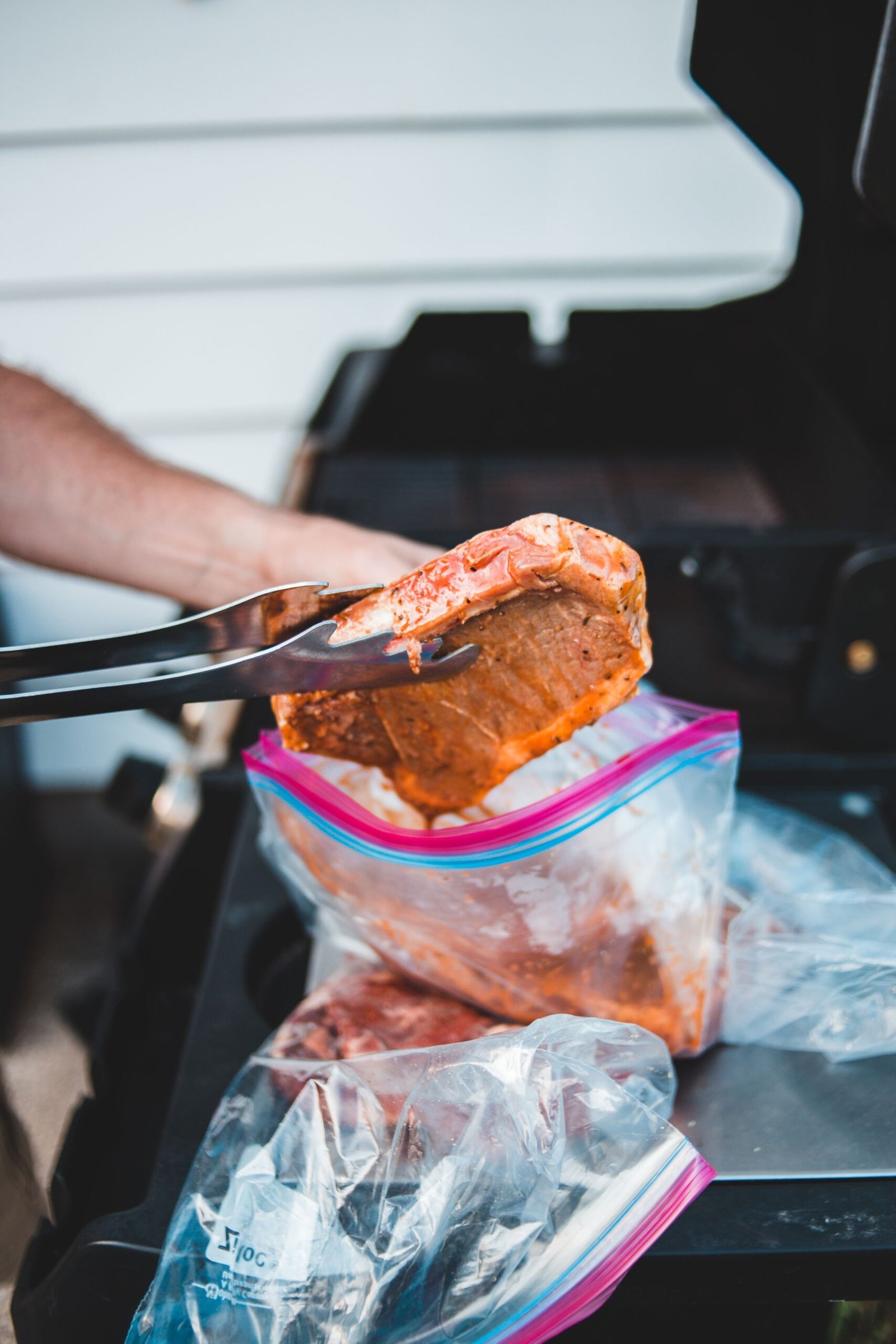 Marinated meat being prepared with tongs before grilling