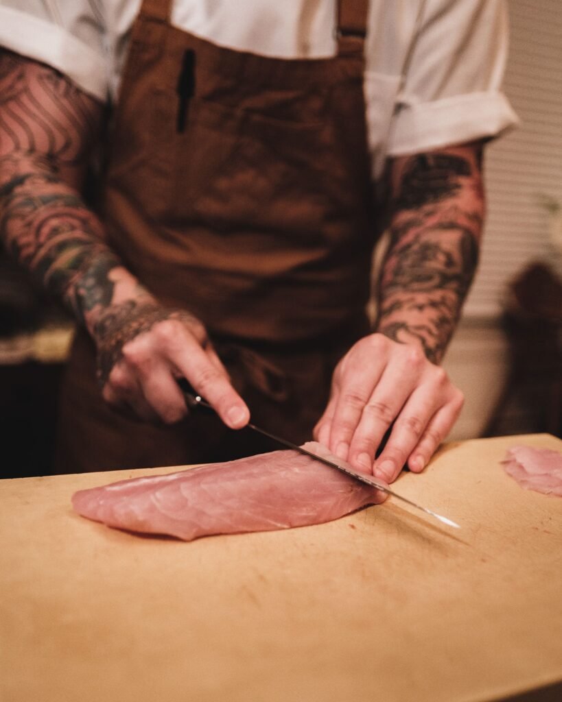 chef slicing raw meat thin with a knife on a cutting board
